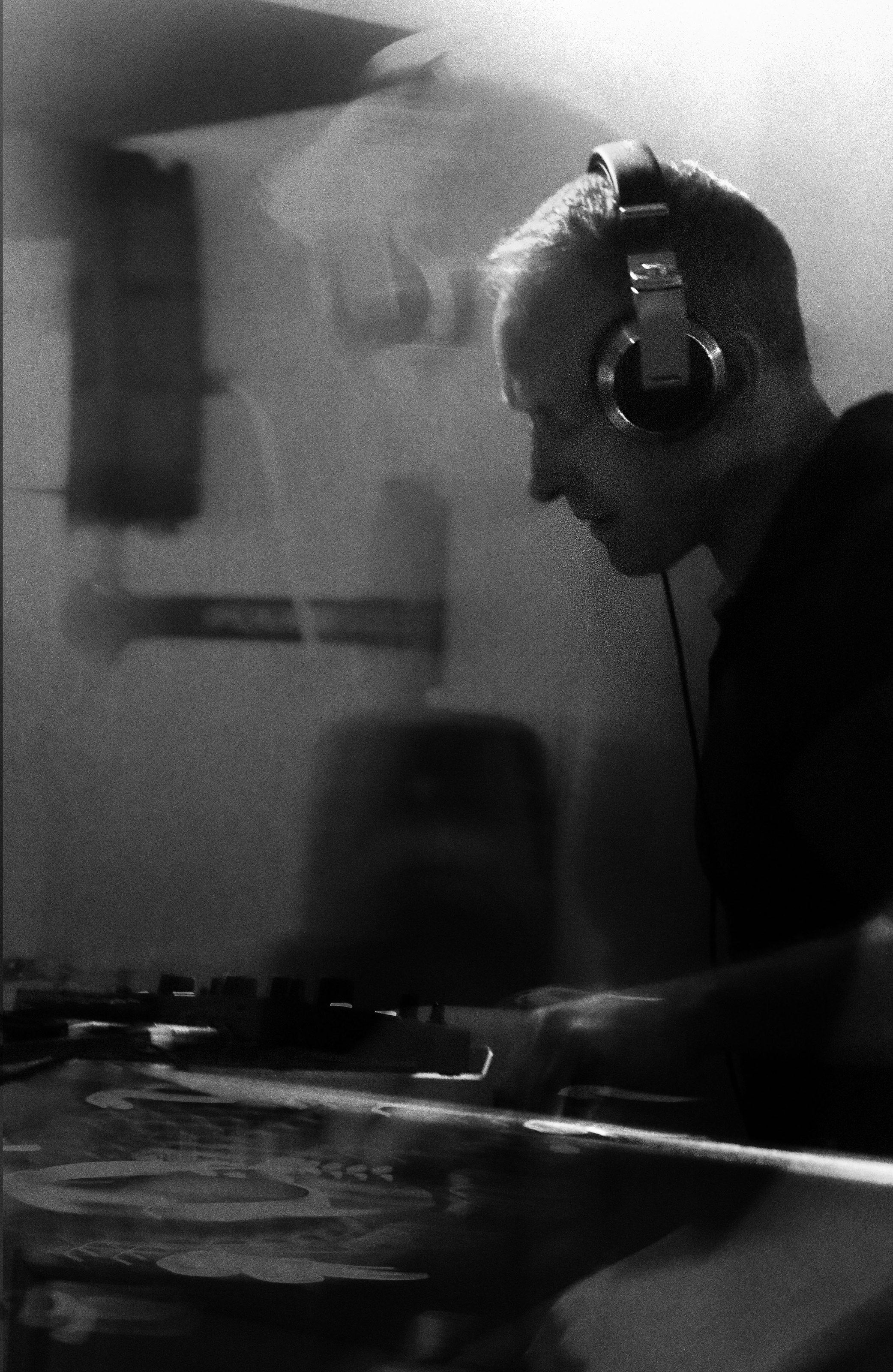 Black-and-white photo of Freshwest in profile at the decks, wearing headphones