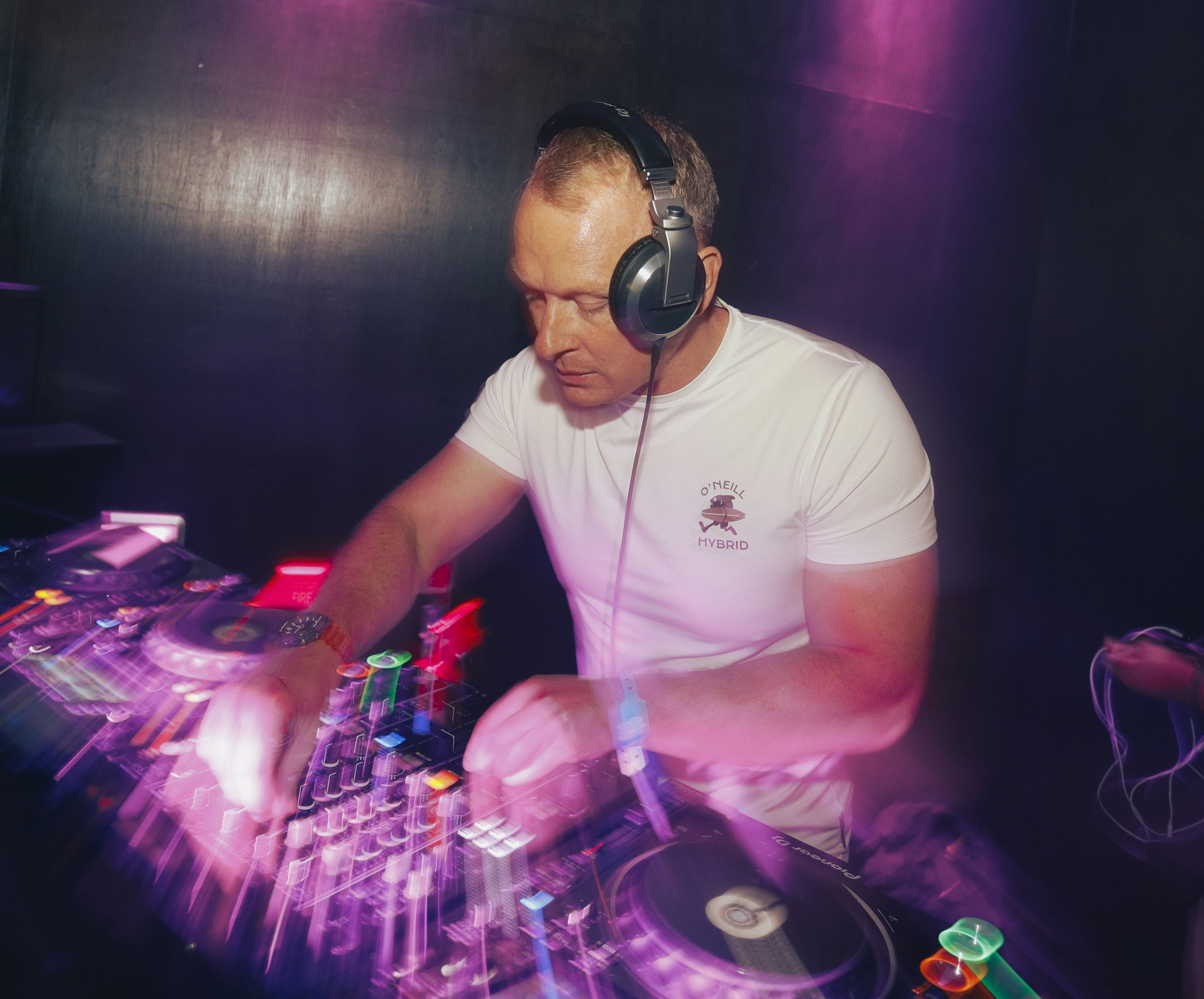 Freshwest mixing at the decks in headphones, lit in purple and pink