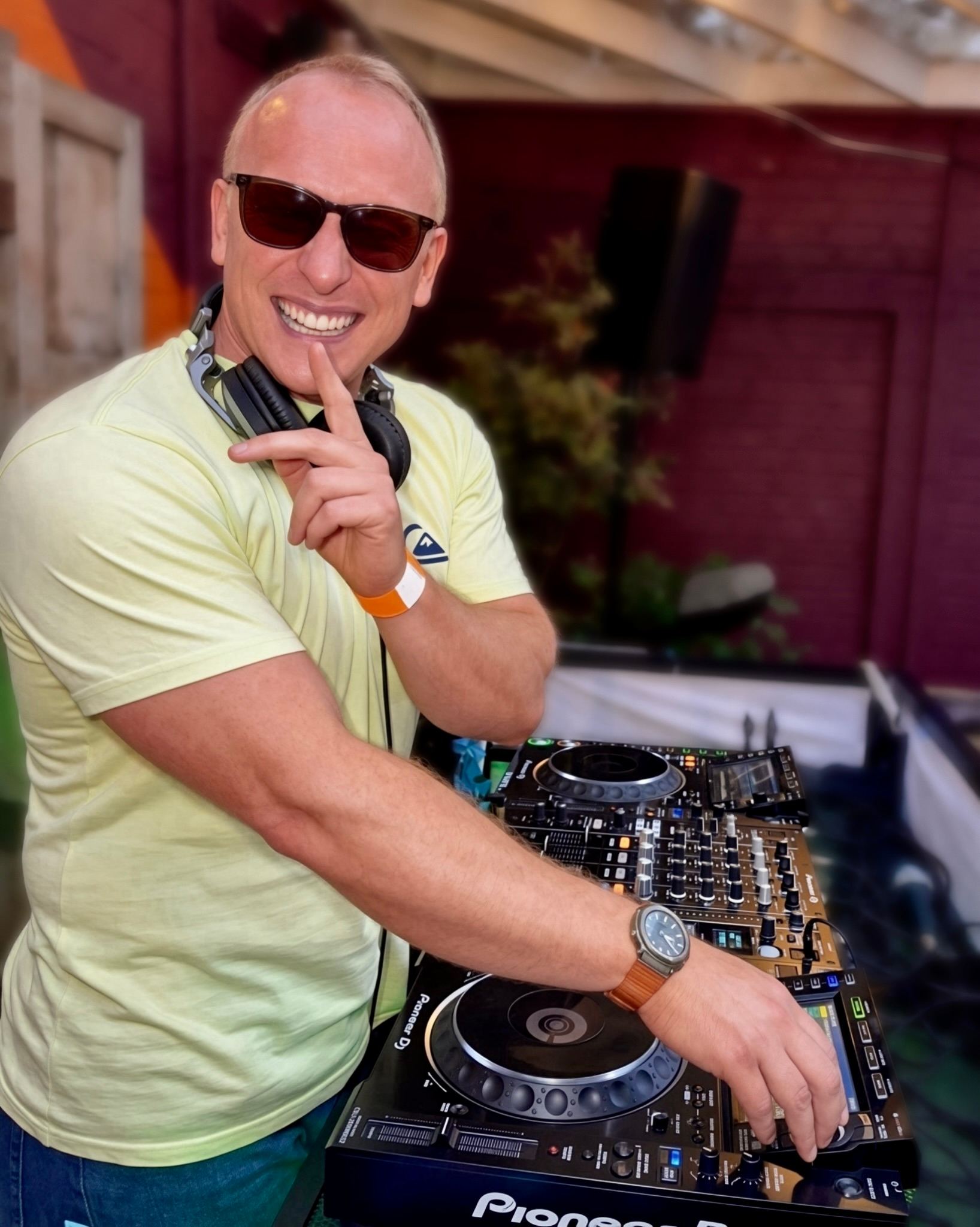 Freshwest smiling at the decks in sunglasses, headphones round his neck
