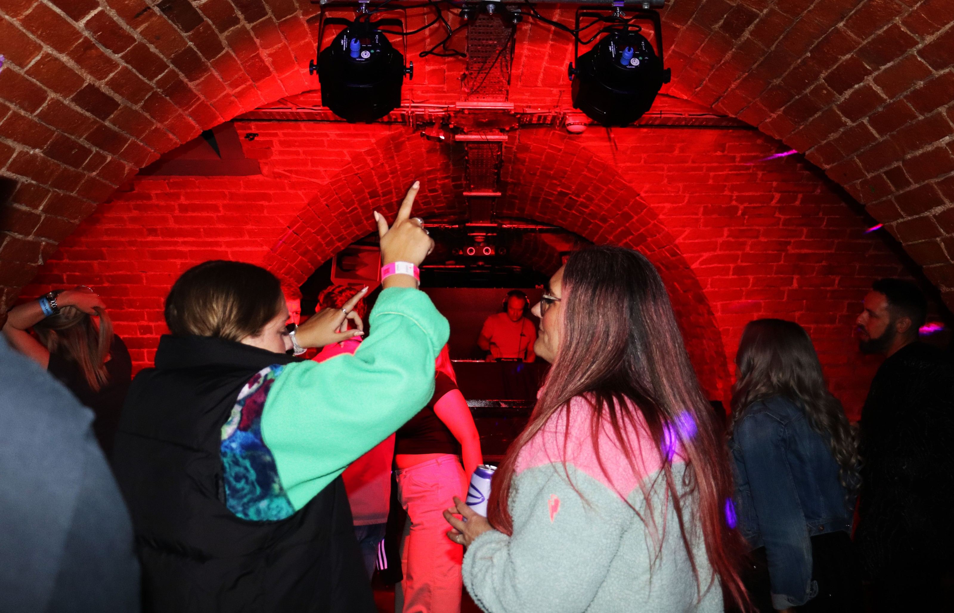 Dancers under red-lit brick arches at a RUN SY1 event, the DJ booth at the far end