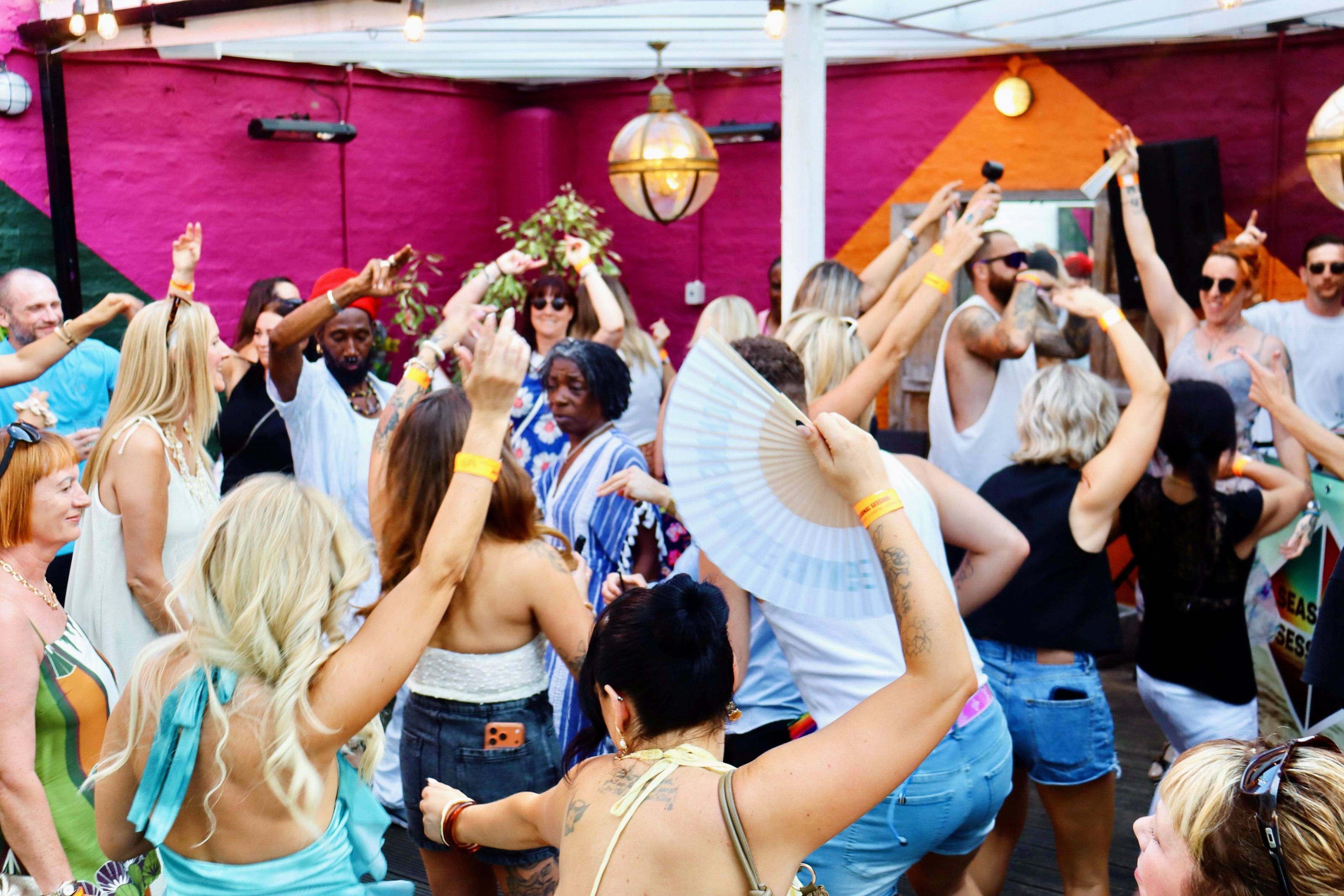 The crowd at Seasunal Sessions Endless Summer dancing with arms raised under a pergola, one dancer holding a fan