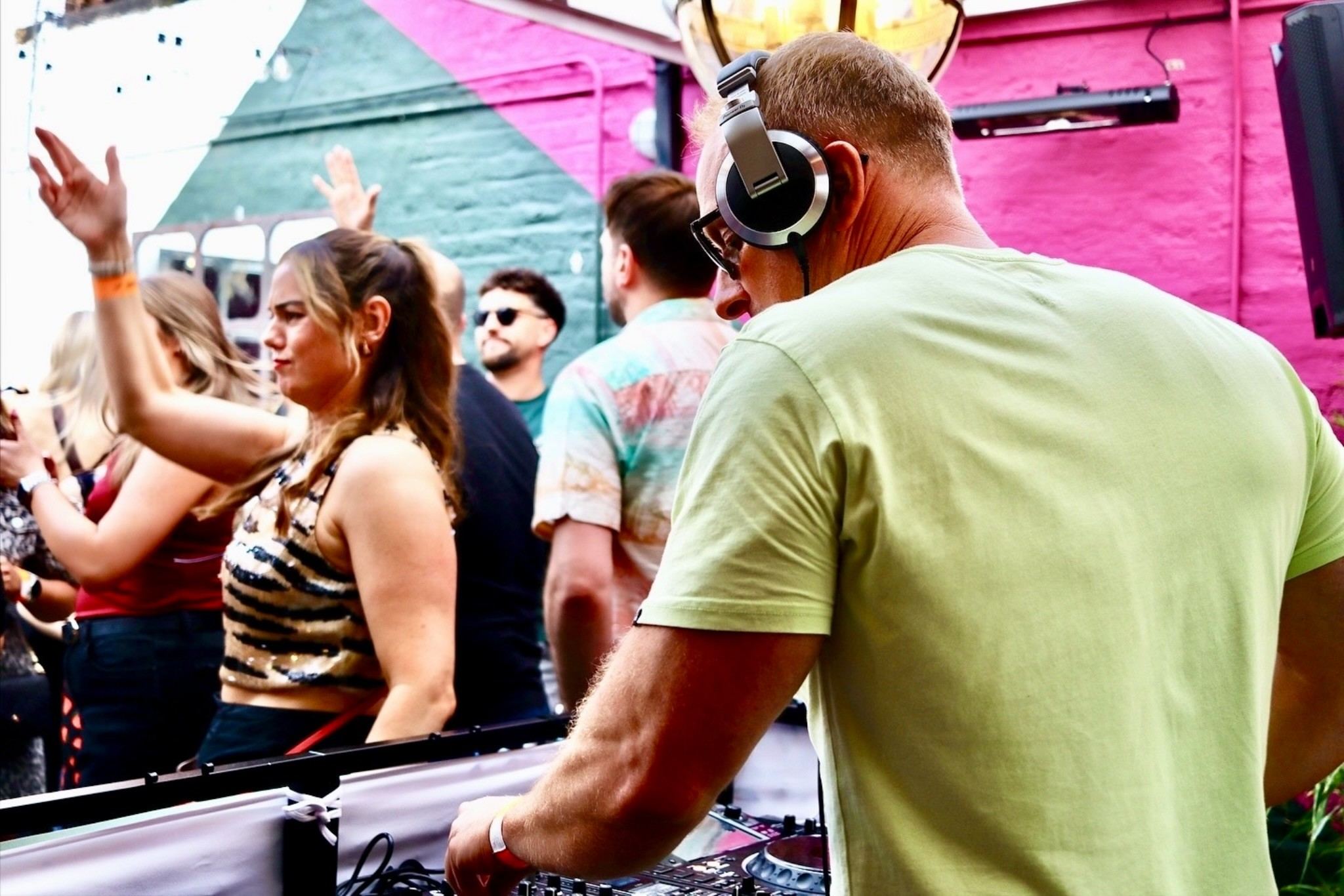 Freshwest on the decks at a Seasunal Sessions event, dancers beside the booth against a painted pink wall