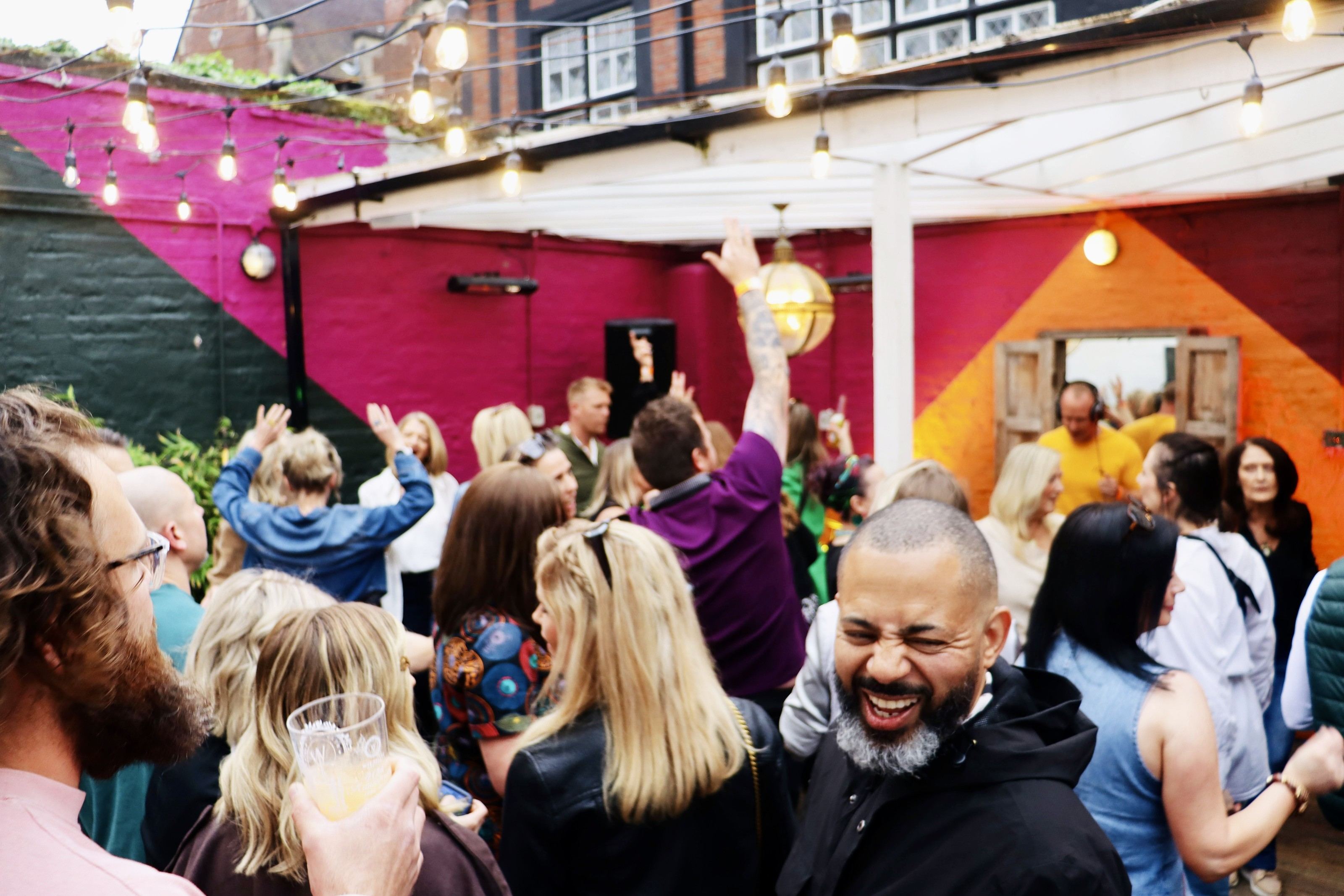 A laughing crowd in a painted courtyard at Seasunal Sessions Spring Safari, the DJ in the doorway behind