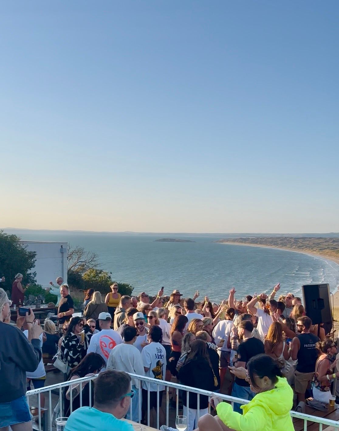 A crowd dancing on the terrace at The View, Rhossili, in early evening light, with Rhossili Bay and Worms Head beyond
